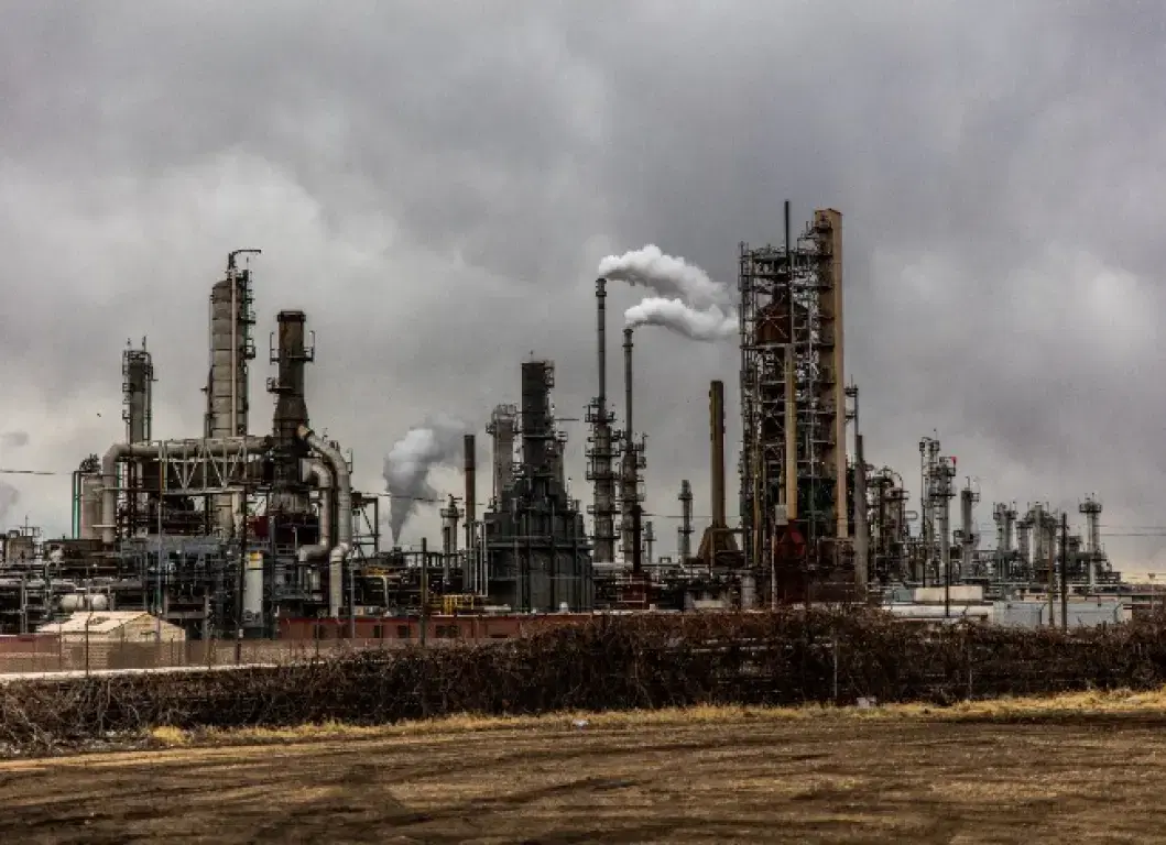 A refinery’s process columns and stacks venting white steam under a grey sky.